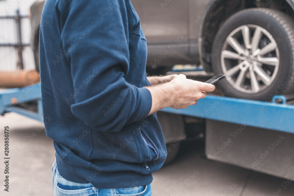 Man with mobile phone.Tow truck with worker towing a broken down car on the highway. Selective focus. Concept