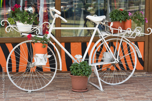 Decorative, vintage bike, painted white, used as a stand for flowerpots. stands in the city center