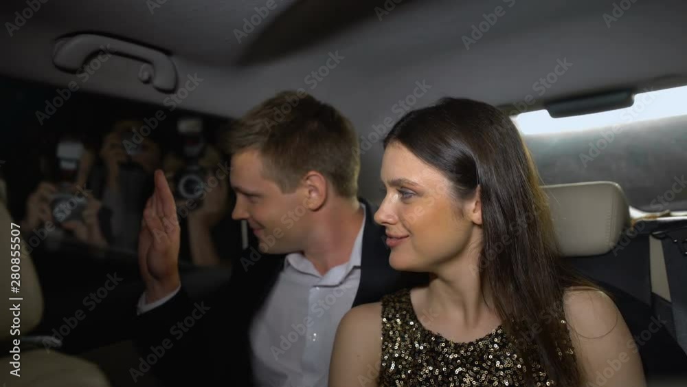 Smiling star couple looking at paparazzi from car, enjoying fame and glory Smiling star couple looking at paparazzi from car, enjoying fame and glory