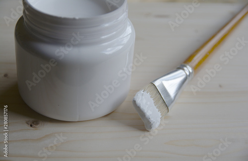 Plastic can with white acrylic primer and a bristle brush on a wooden panel. Preparing the surface for drawing.