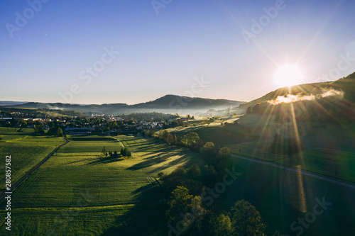 aerial shot of beautiful green field with morning dew during sunny day in the countryside of switzerland, peaceful relaxing drone shot