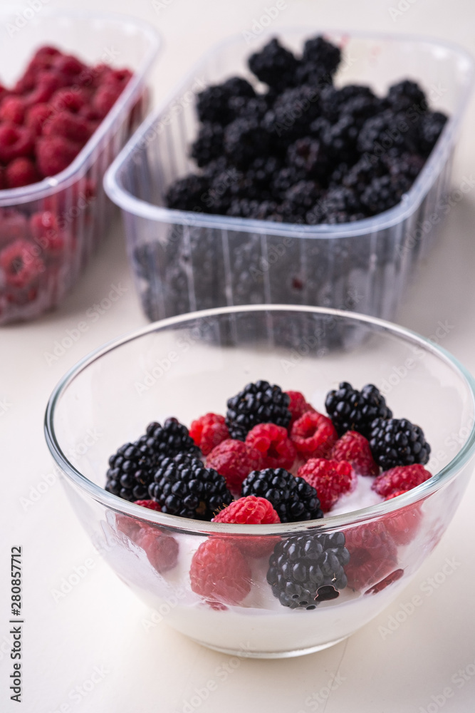 Ice cream with raspberry, blackberry in glass bowl near two containers of berries on white background Ice cream with raspberry, blackberry in glass bowl near two containers of berries on white background