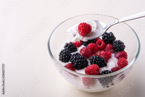 Ice cream with raspberry, blackberry berries with spoon in glass bowl on white background