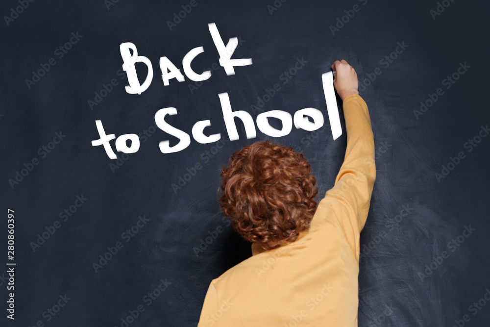 Child writing boy Back to school text on chalkboard background