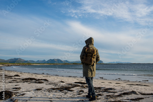 A man with backpack walking along empty ocean beach on sunset. Harmony with nature, relaxation. Scenic view. Travel, adventure. Sense of freedom, lifestyle. Explore North Norway. Summer in Scandinavia