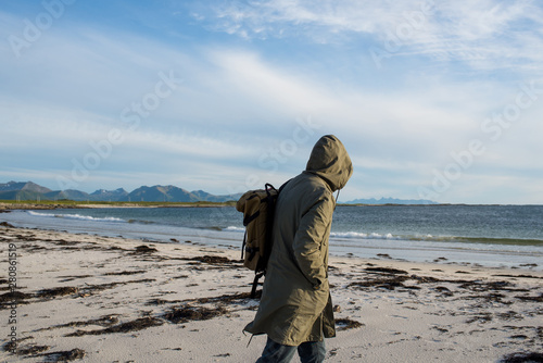 A man with backpack walking along empty ocean beach on sunset. Harmony with nature, relaxation. Scenic view. Travel, adventure. Sense of freedom, lifestyle. Explore North Norway. Summer in Scandinavia