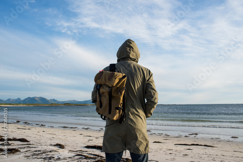 A man with backpack walking along empty ocean beach on sunset. Harmony with nature, relaxation. Scenic view. Travel, adventure. Sense of freedom, lifestyle. Explore North Norway. Summer in Scandinavia © Iuliia Pilipeichenko