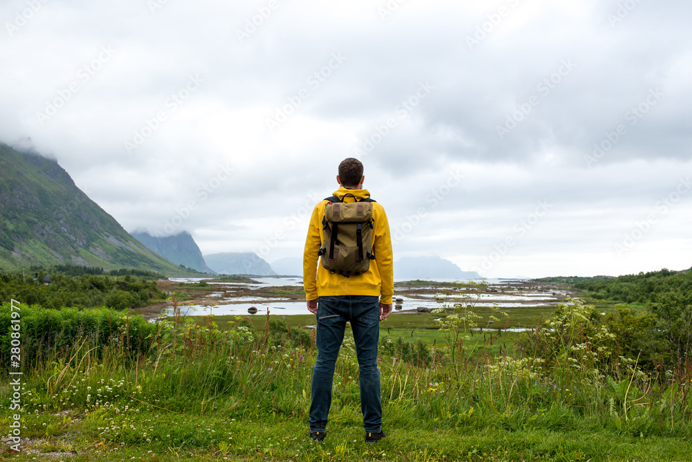 Men in yellow hoodie with backpack enjoys the scenic view of the fjord. Stunning beauty nature. Harmony, relax lifestyle. Travel, adventure. Sense of freedom. Explore North Norway. Scandinavia summer 