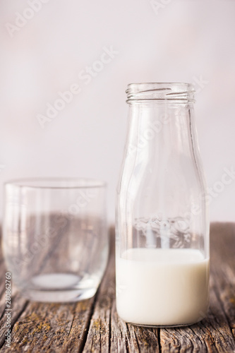 Semi-empty bottle of milk, next to empty glass, on rustic wooden table