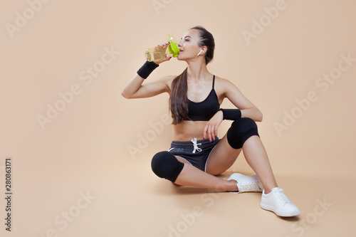 Athletic brunette girl, in sports uniform, sits, rests after a workout, with a bottle in her hand, drinking water.