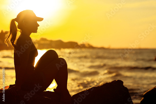 Profile of a relaxed calm woman silhouette sitting on the miami beach and watching sunset