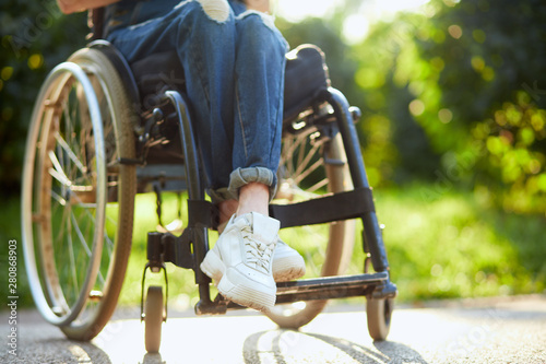 Obraz na plátně young disabled girl in overall and white trainers sitting with crossed legs on the wheelchair