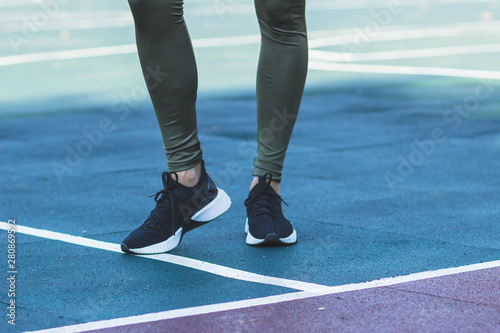 Woman in sneakers and sport clothes makes sport exercises on the athletic field, blurred background