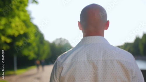 Rear view of bald man standing in a park and looking ahead. Close up shot.