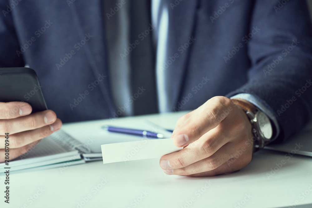 Mid section of businessman in suit holding blank business card and dialing numbers on mobile phone. Mid section of businessman in suit holding blank business card and dialing numbers on mobile phone.