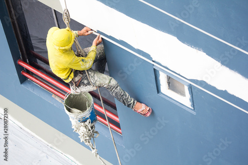 painters hanging on roll, painting color on building wall.