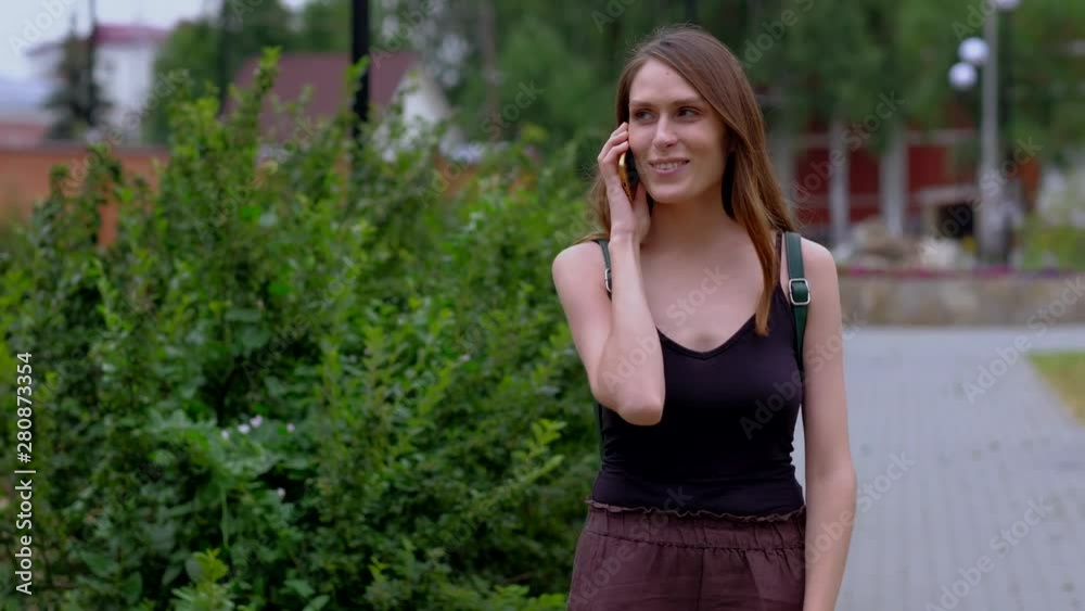 Pretty brunette girl with good mood walking and talk on smartphone and smiling in park. Pretty brunette girl with good mood walking and talk on smartphone and smiling in park.