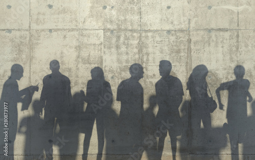 Group of people walking in a relaxed pose cast a shadow on the concrete wall. Conceptual creative illustration with silhouettes of men and women. Copy space. 3D rendering.