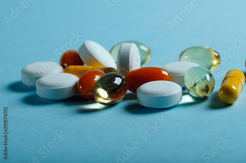 A lot of bright pills of drugs on a blue background. Cropped shot, horizontal, side view. The concept of medicine and health. Crisis opioid painkiller and drug addiction concept.