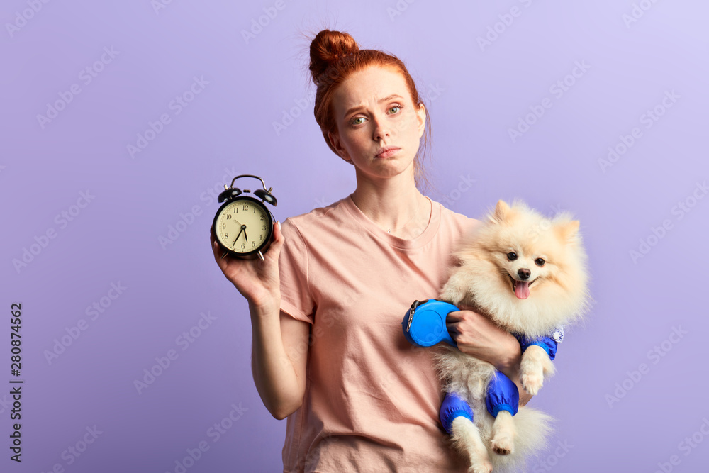 beautiful young sleepy unhappy woman holding a clock and her dog in ...