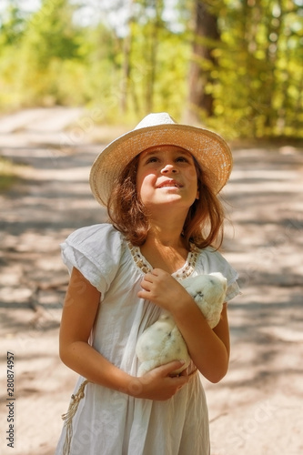 Girl child in white dress and hat walking in the summer forest