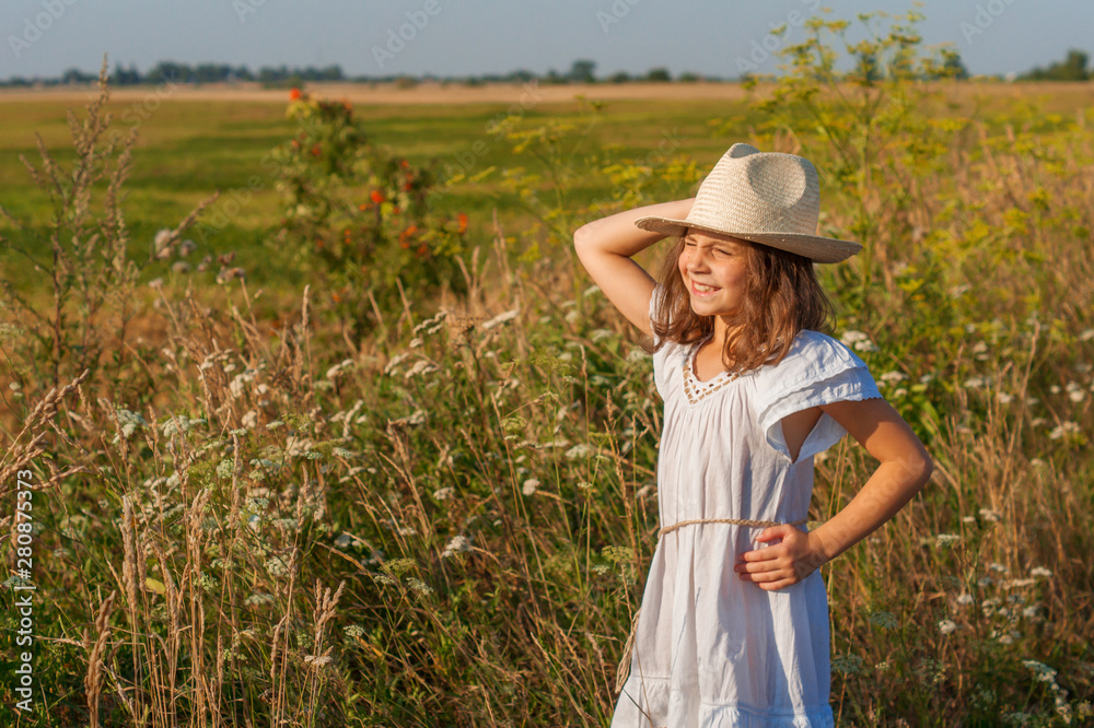 Child girl in a white dress and a hat on a farm summer field.