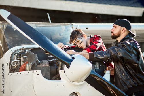 view of young aircraft male engineer with his son making together trouble-shooting of small single-engine propeller plane, kid fixing engine with screwdriver while dad teaching him.