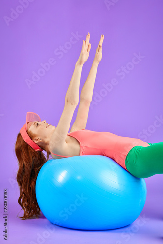 slim young pretty woman laying down on blue fitness ball with hands up and looking above with smile, trains endurance and strength, demonstrates good flexibility. Fitness and health concept.