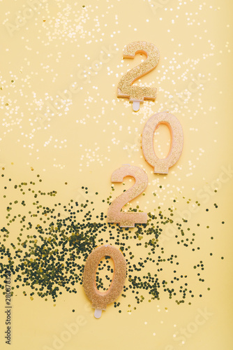 Let's celebrate new New Years Eve celebration background with champagn glass, 2020 number made with golden glitter candles, christmas decoration around, flatlay over a golden board, luxury holiday co