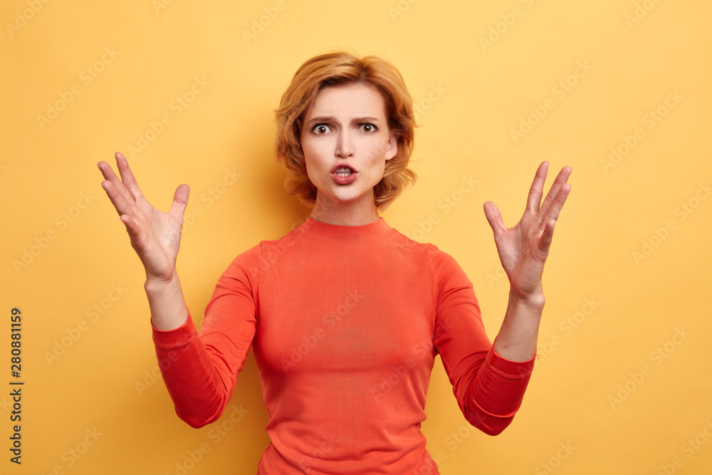 Fototapeta premium angry irritated frustrated woman with hands raised shouting at camera isolated on the yellow background. close up portrait, studio shot. feeling , emotion, facial expression