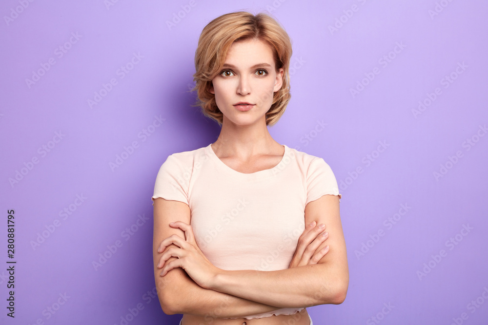 serious beautiful woman dressed casually keeping arms folded, looking at camera with strict face. isolated blue background