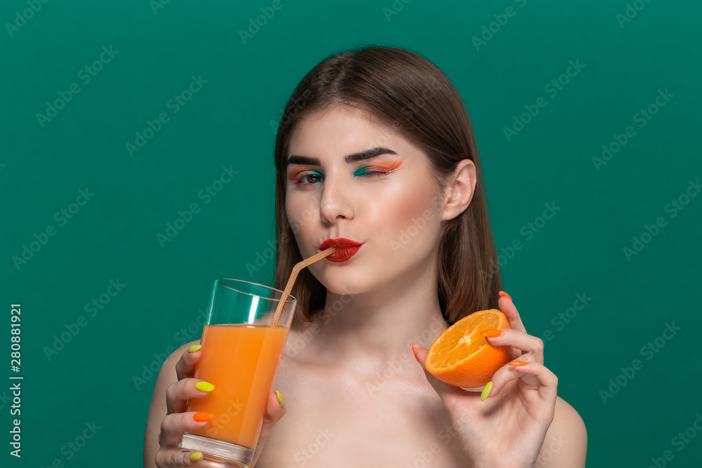 Closeup portrait of beautiful young woman with bright color make-up drinking orange juice and holding half of an orange Closeup portrait of beautiful young woman with bright color make-up drinking orange juice and holding half of an orange