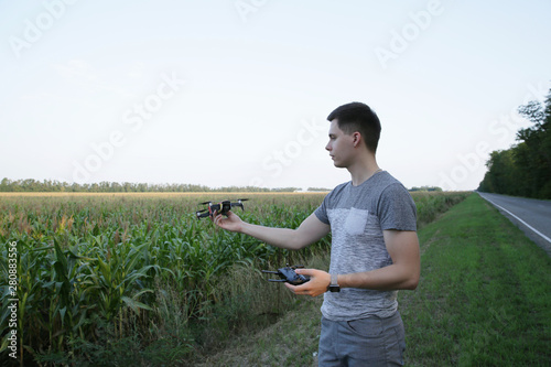 active young man uses a quad drone to fly around a cornfield. He controls the drone with a remote control. The concept of new technologies and innovations in agriculture.