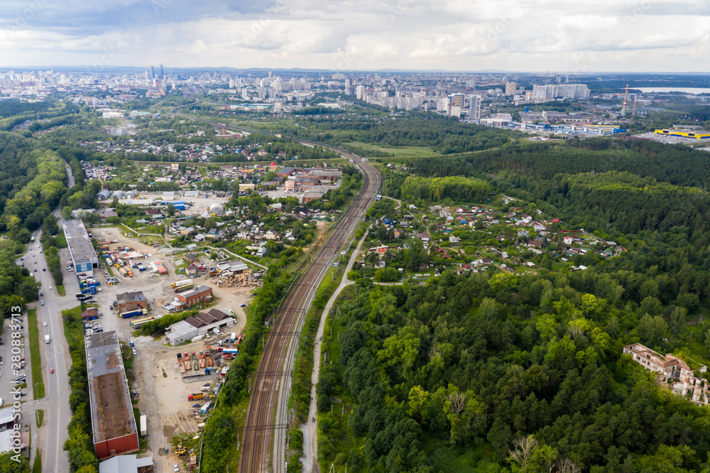 The city skyline in the distance in foreground, railway, industrial area and a forest with houses. Yekaterinburg, Russia