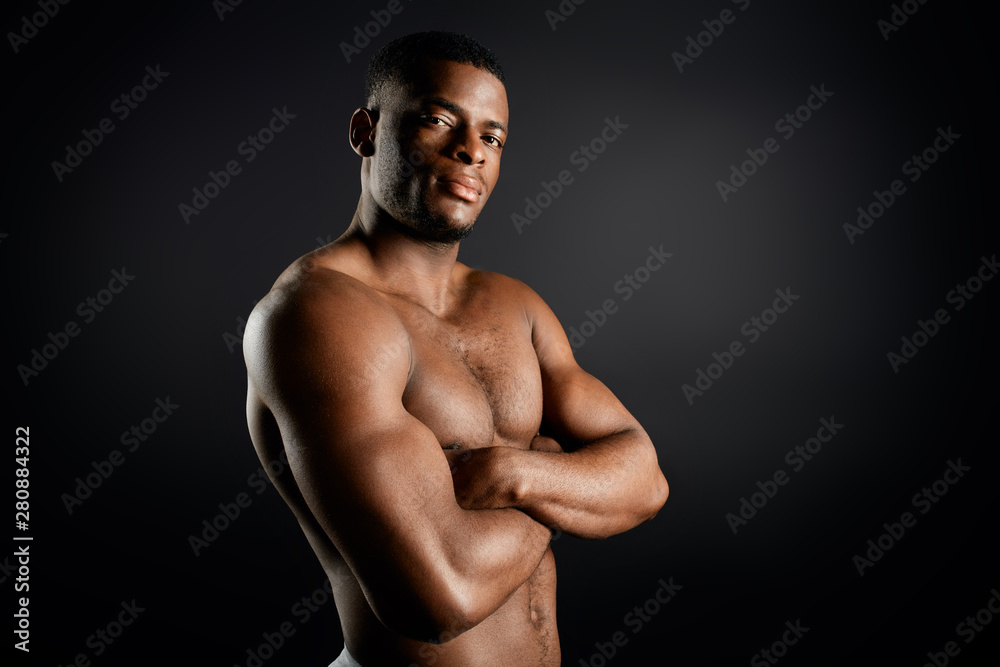 confident serious personal trainer with folded arms posing to the camera, isolated black background. confidence concept. copy space