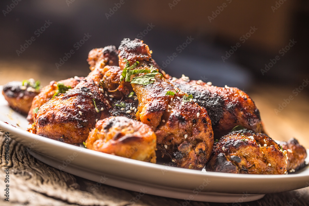 Grilled hicken legs BBQ with spices herbs and sesame on baked paper. Roasted poultry meal on white plate Grilled hicken legs BBQ with spices herbs and sesame on baked paper. Roasted poultry meal on white plate