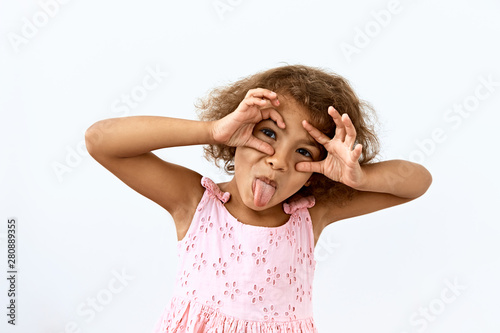 Making face,funny  foolishes portrait of little African American girl, against white background.