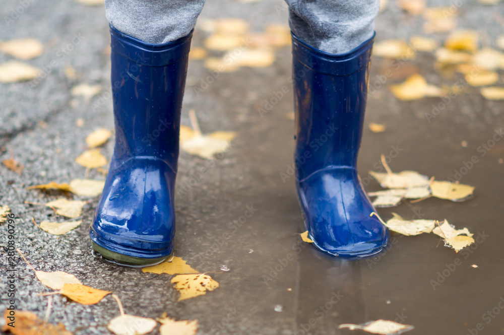 Feet of child in blue rubber boots jumping over a puddle after the rain. Close up of child wellies in autumn weather
