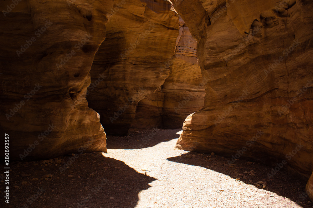 Red canyon desert scenic landscape narrow path way trail between steep sand stone bare rocks, big contrast with lights and shadows and summer Middle East hot season weather time 