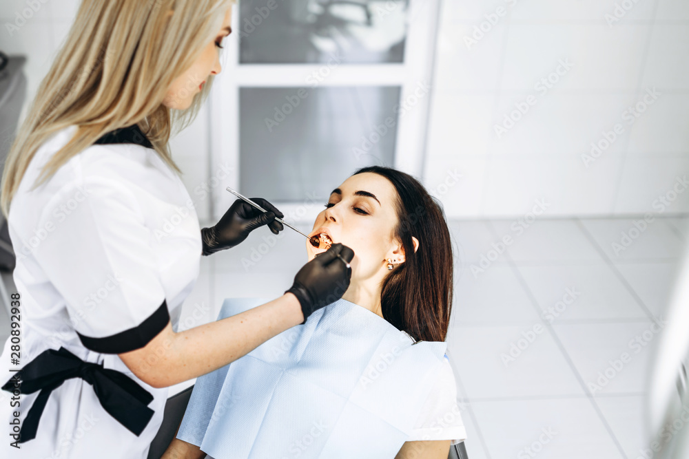 Pretty young female dentist making examination and treatment for young female patient in dental clinic. Pretty young female dentist making examination and treatment for young female patient in dental clinic.
