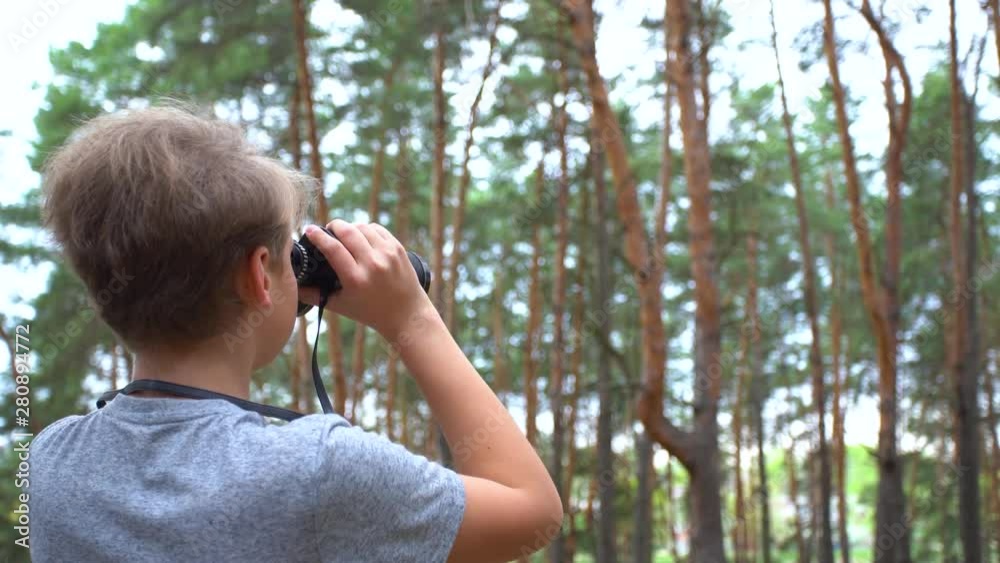 Closeup back view of white kid looking through black vintage binoculars at something in distance in green pine forest. Real time 4k video footage. Closeup back view of white kid looking through black vintage binoculars at something in distance in green pine forest. Real time 4k video footage.