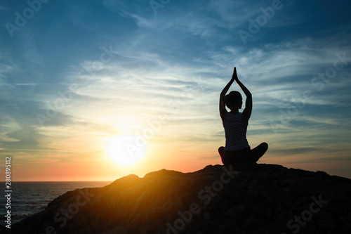 Yoga woman meditating in the Lotus position. Silhouette on the sea coast during amazing sunset.