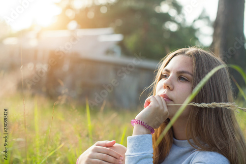 Teenage girl sitting in green grass in summer countryside at sunlight.