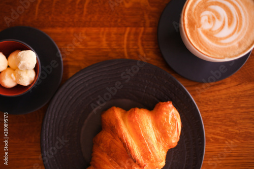 Baked croissant on a black plate with a white coffee cup, cup of butter on the wooden background. Breacfast bakery restaurant lifestyle. photo