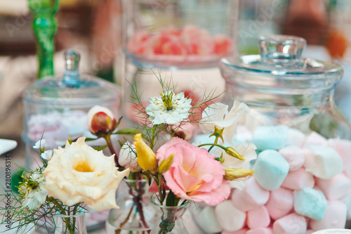 Close-up of a bouquet of summer flowers against a vase of marshmallows and a picnic table set, selective focus