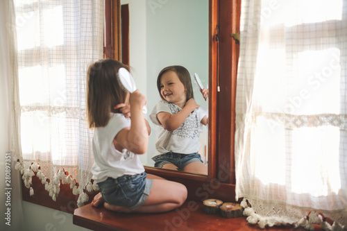 funny girl child combing hair in front of mirror