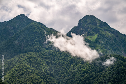 Green slopes and rocky peaks of high mountains in cloudy summer day