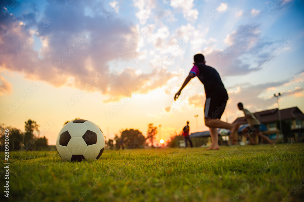 Action sport outdoors of kids having fun playing soccer football for exercise in community rural area under the twilight sunset sky. Fresh silhouette and vibrant image with anonymous people.