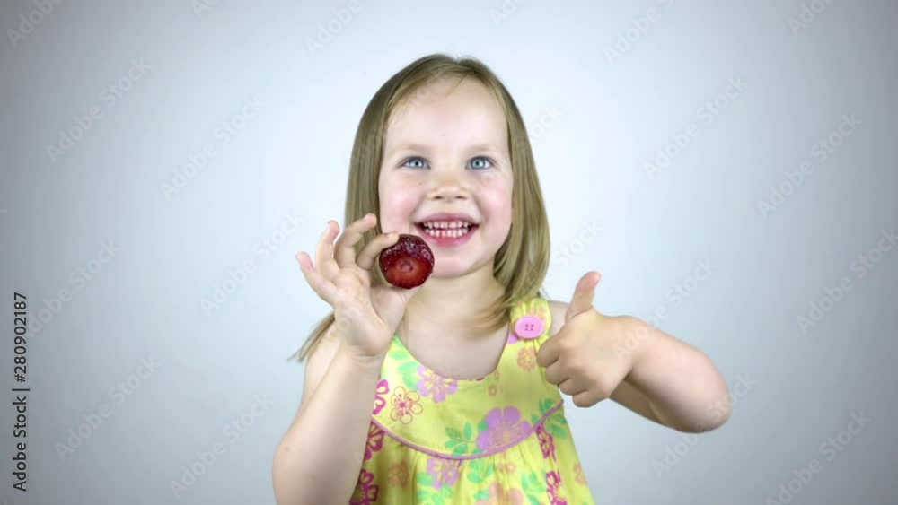 A three year old child girl eats strawberries and shows thumb up. Smiles. A three year old child girl eats strawberries and shows thumb up. Smiles.