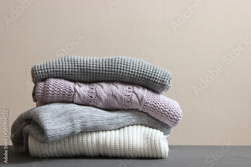 A pile of warm sweaters on a wooden table on a color background. Autumn and winter clothes.